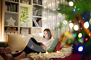 Cute young girl using a tablet pc at home in warm and cozy living room at Christmas. Family having online video call on Xmas eve