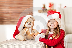 Cute young girl wearing santa hat holding her christmas present, soft toy teddy bear. Happy kid with xmas present.