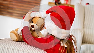 Cute young girl wearing santa hat playing with her christmas present, soft toy teddy bear. Happy kid with xmas present.