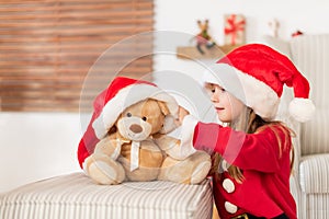 Cute young girl wearing santa hat playing with her christmas present, soft toy teddy bear. Playful kid at christmas time.