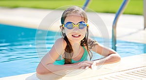 Cute young girl wearing swimming goggles having fun in outdoor pool. Child learning to swim. Kid having fun with water toys photo