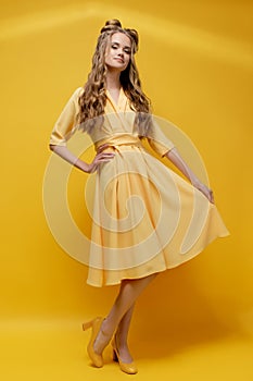 Cute young girl in a yellow dress on a yellow background with a haircut and curly long hair.