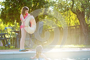 Cute young girls having fun in outdoor pool. Children learning to swim. Kids having fun with water toys. Family fun in a pool.