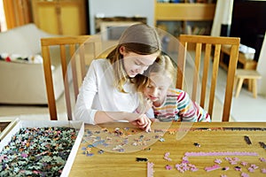 Cute young girls playing puzzles at home. Children connecting jigsaw puzzle pieces in a living room table. Kids assembling a