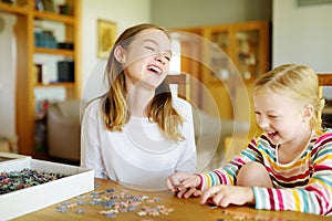 Cute young girls playing puzzles at home. Children connecting jigsaw puzzle pieces in a living room table. Kids assembling a photo