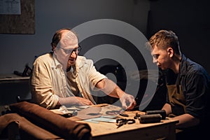 a cute young guy wants to make a gift with his own hands, an experienced shoemaker helps him make shoes out of leather.