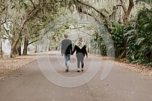 Cute Young Happy Loving Couple Walking Down an Old Abandoned Road with Mossy Oak Trees Overhanging