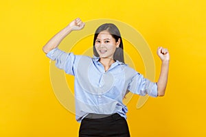 Cute and young Japanese style girl standing and raise hand show fist punches with smile face on yellow background