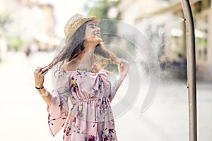 A cute young lady is relaxing from the heat under a water shower in the city center