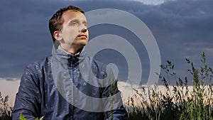 A cute young man admires nature at sunset on the field. Beautiful sky on a background.