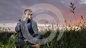 A cute young man drinks a hot drink at sunset on the field. Beautiful sky on a background.