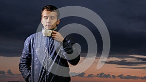 A cute young man drinks a hot drink at sunset on the field. Beautiful sky on a background.