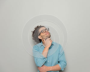 cute young man with glasses touching chin, looking up and dreaming