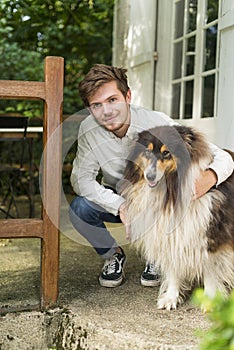 Cute young man kneeling with hairy collie dog outdoors