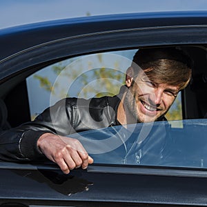 Cute young man smiling and looking out of an open car window.