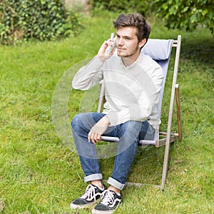 Cute young man with telephone sitting in the garden