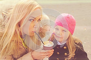 Cute young mother with daughter have a fun drinking a milkshake from the same paper cup.