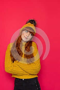 Cute young red haired woman in hat with pompom is looking up