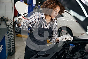 Cute young repairwoman checks the oil level in the car