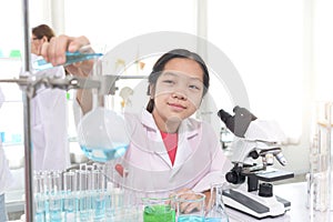 Cute young scientist schoolgirl in lab coat do science experiments. Student girl use equipment to study chemistry in school