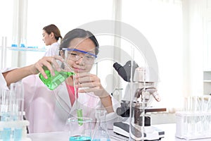 Cute young scientist schoolgirl in lab coat do science experiments. Student girl use equipment to study chemistry in school