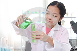 Cute young scientist schoolgirl in lab coat doing science experiments in laboratory. Student girl child pouring green reagent