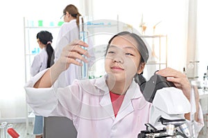 Cute young scientist schoolgirl in lab coat show blue chemical test tube. Student girl child use lab equipment to do science