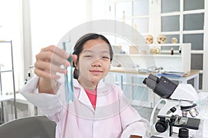 Cute young scientist schoolgirl in lab coat show blue chemical test tube. Student girl child use lab equipment to do science