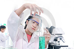 Cute young scientist schoolgirl wearing lab coat and safety glasses, doing science experiments. Student girl child using lab