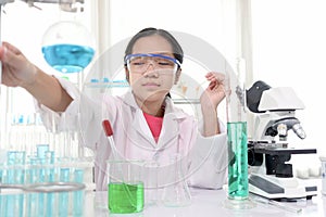 Cute young scientist schoolgirl wearing lab coat and safety glasses, doing science experiments. Student girl child using lab