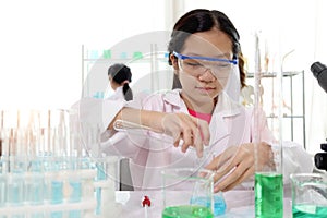 Cute young scientist schoolgirl wearing lab coat and safety glasses, doing science experiments. Student girl child using lab