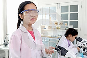 Cute young scientist schoolgirl wearing lab coat and safety glasses, doing science experiments. Student girl child using lab
