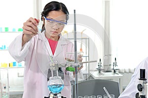 Cute young scientist schoolgirl wearing lab coat and safety glasses, doing science experiments. Student girl child using lab