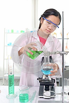 Cute young scientist schoolgirl wearing lab coat and safety glasses, doing science experiments. Student girl child using lab