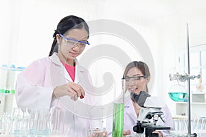 Cute young scientist schoolgirl wears lab coat and safety glasses, doing science experiments under guidance of teacher. Student