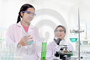 Cute young scientist schoolgirl wears lab coat and safety glasses, doing science experiments under guidance of teacher. Student