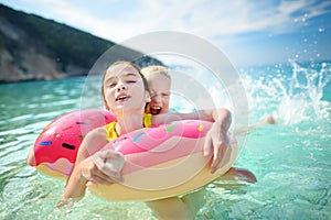 Cute young sisters floating on toy ring at Myrtos beach, the most famous and beautiful beach of Kefalonia, a large coast with