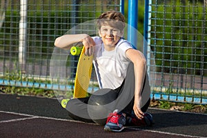 Cute young sport boy with yellow skateboard. He has a good time on his free time on weekend, holidayson sports ground.