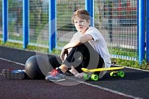 Cute young sport boy with yellow skateboard. He has a good time on his free time on weekend, holidayson sports ground.