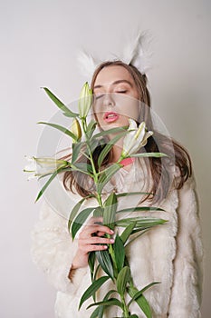 Cute young teen girl standing in a winter warm fur coat and cat furry ears on her head, she holds a branch of fresh lilies. woman
