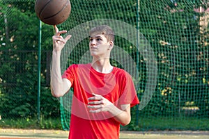Cute young teenager in red t shirt with a ball plays basketball on court. Teenager dribbling the ball, running in the stadium.