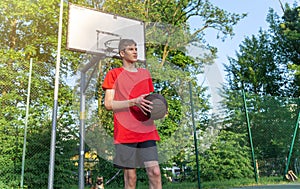 Cute young teenager in red t shirt with a ball plays basketball on court. Teenager dribbling the ball, running in the stadium.