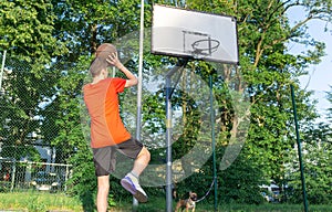 Cute young teenager in red t shirt with a ball plays basketball on court. Teenager dribbling the ball, running in the stadium.