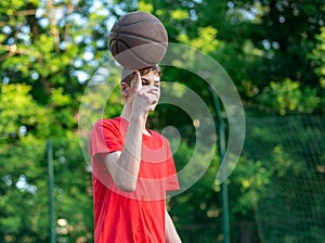 Cute young teenager in red t shirt with a ball plays basketball on court. Teenager dribbling the ball,  running in the stadium.
