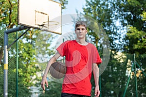 Cute young teenager in red t shirt with a ball plays basketball on court. Teenager dribbling the ball,  running in the stadium.