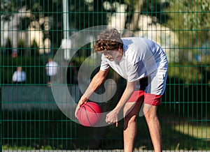 Cute young teenager in t shirt with a ball plays basketball on court. Sports, hobby, active lifestyle for boys