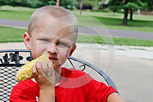 Cute young toddler boy eating an ear of corn