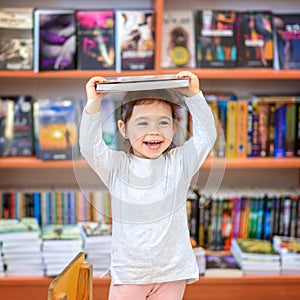 Cute Young Toddler Standing and Holding Book in Head. Child in a Library, Shop,Bookstore.