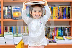 Cute Young Toddler Standing and Holding Book in Head. Child in a Library, Shop,Bookstore.