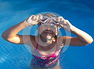 Cute young well-tanned girl in the pool takes off or puts on her diving mask.